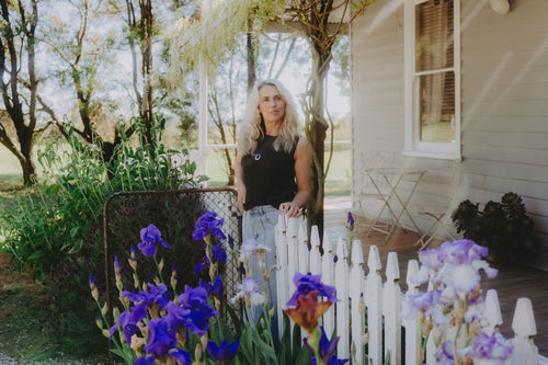 Woman wearing a charcoal alpaca vest and denim skirt, standing in a cottage garden