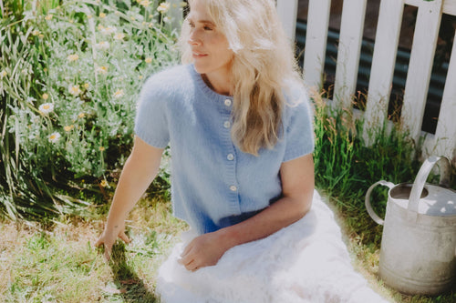 A woman wears a short sleeve suri alpaca cardigan, styled as a top with a white skirt